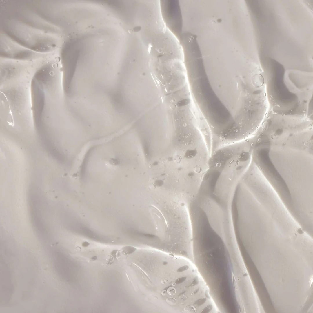 Un gros plan sur un liquide blanc, onctueux et lisse, parsemé de légères ondulations et de petites bulles, met en valeur la texture douce et brillante du gel douche pour homme « Le Petit Olivier » Vivifiant - Fraîcheur Marine.