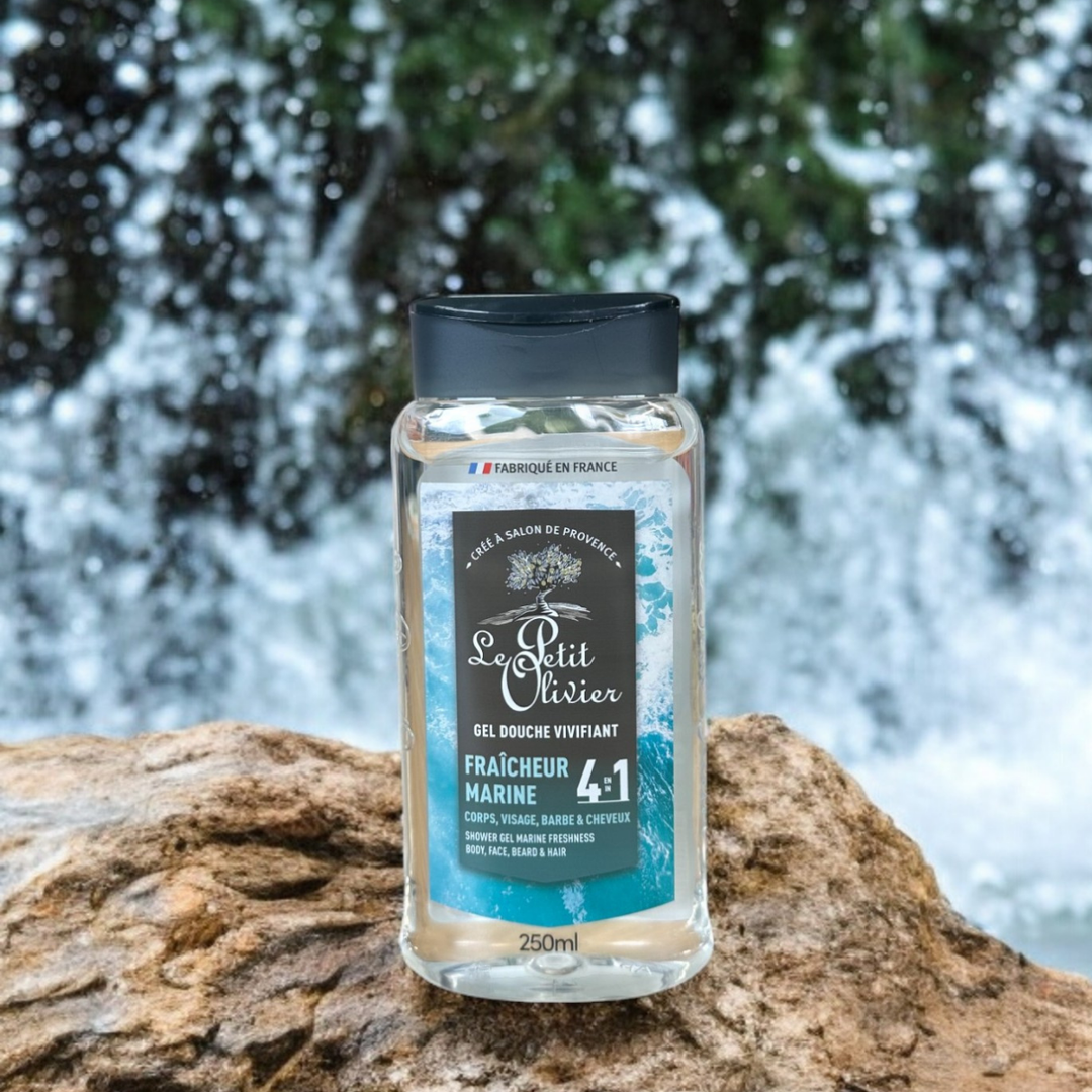 Un flacon de gel douche pour homme « Le Petit Olivier – Vivifiant – Fraîcheur Marine » repose sur un rocher, avec une cascade et de la végétation en arrière-plan, le tout flou. Son étiquette bleue et noire comporte un texte en blanc et bleu clair.