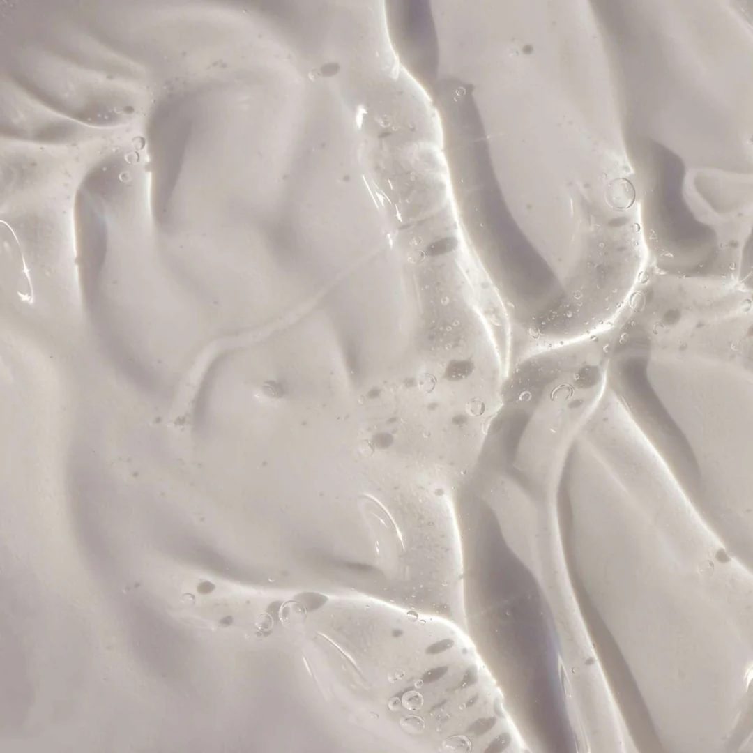 Un gros plan sur un liquide lisse, d'un blanc laiteux, parsemé de légères ondulations et de bulles, qui rappelle le gel douche pour homme « Énergisant - Fraîcheur Boisée » de Le Petit Olivier, crée un effet abstrait aux reflets délicats.