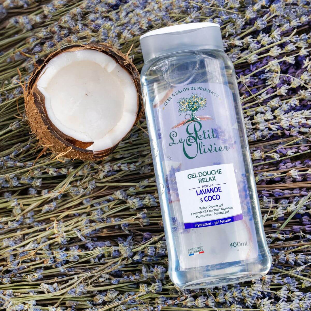 Un flacon de gel douche Relax « Le Petit Olivier » est posé sur des fleurs de lavande séchées, à côté d'une noix de coco coupée en deux.