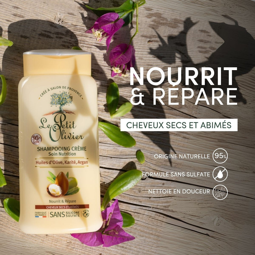 Un flacon de « Le Petit Olivier – Shampooing pour cheveux secs et abîmés » repose sur un fond de bois orné de feuilles vertes et de fleurs violettes, mettant en avant son action nourrissante pour les cheveux secs grâce à des huiles précieuses et à une formule sans sulfate d’origine naturelle.