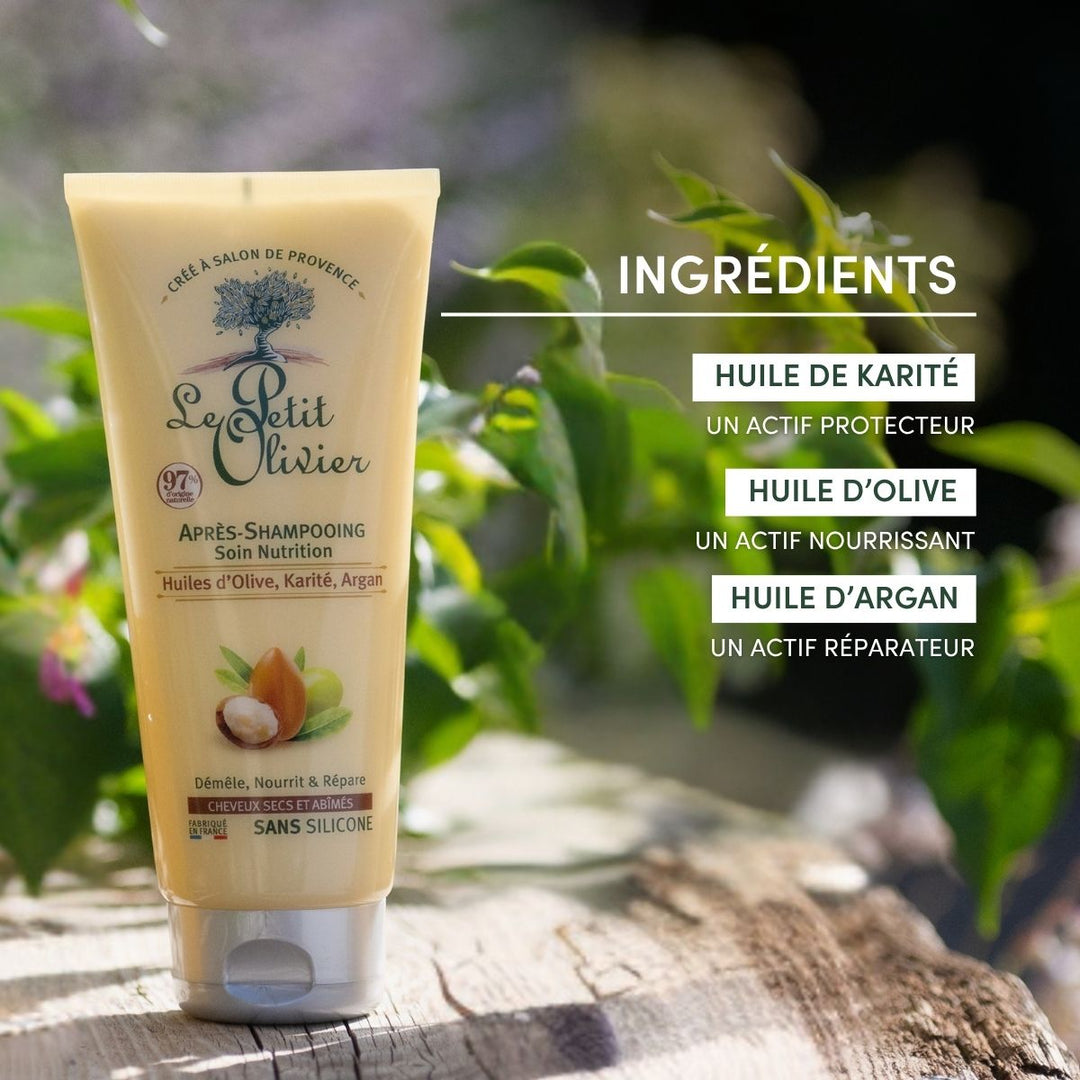 Un tube d'après-shampoing « Le Petit Olivier » pour cheveux secs et abîmés repose sur une pierre à l'extérieur, avec de l'herbe en arrière-plan. Il met en avant des huiles précieuses telles que le beurre de karité et l'huile d'argan, ainsi que sa formule sans silicone destinée aux cheveux secs et abîmés.