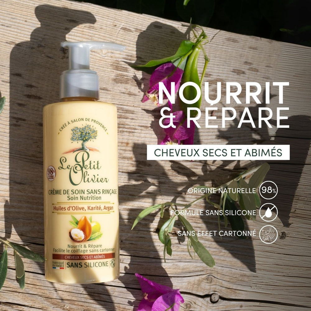 Un flacon de « Le Petit Olivier Crème de Soin Cheveux Secs et Abîmés » repose sur une pierre, entouré de feuilles vertes et de fleurs violettes. Un texte en français met en avant ce soin nourrissant destiné aux cheveux secs et abîmés.
