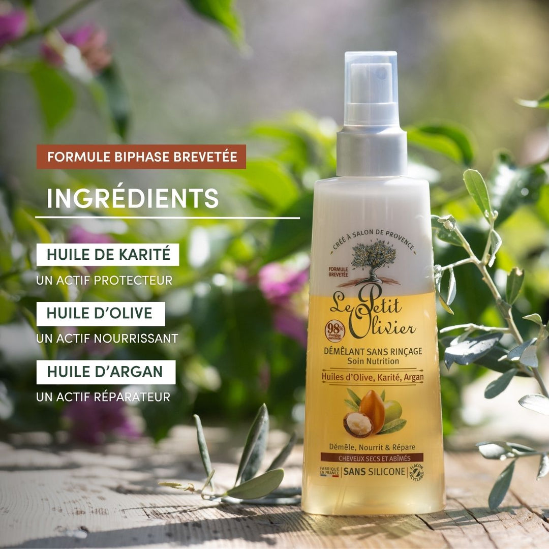 Un flacon de « Le Petit Olivier Spray Démêlant Sans Rinçage Cheveux Secs et Abîmés » repose sur une surface en bois à l'extérieur, au milieu de la verdure — idéal pour nourrir, protéger et réparer les cheveux secs ou abîmés.