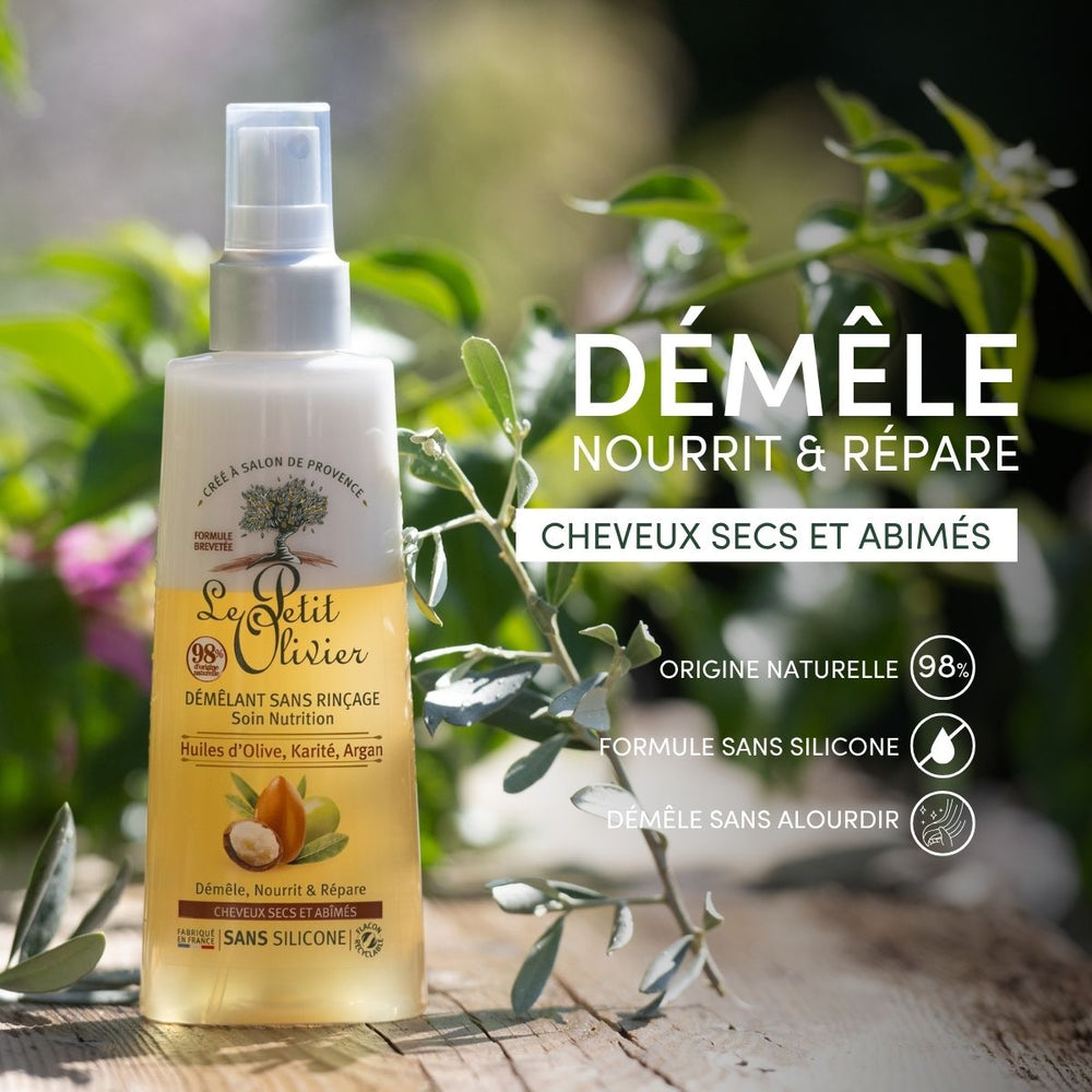 Une bouteille de « Le Petit Olivier Spray Démêlant Sans Rinçage Cheveux Secs et Abîmés » trône au milieu d'un feuillage vert et de fleurs ; son étiquette met en avant son origine naturelle, ses huiles végétales et ses bienfaits pour les cheveux secs et abîmés.