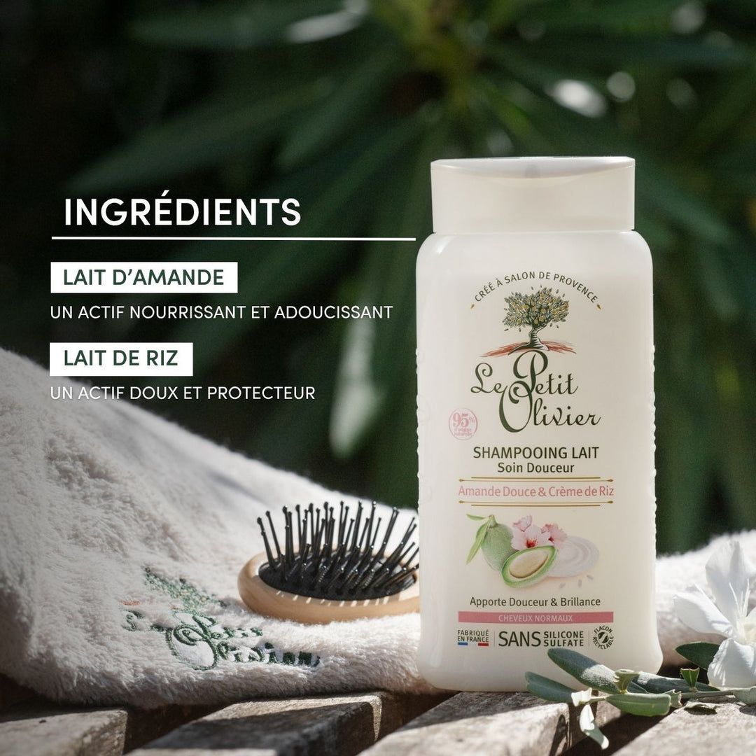 A bottle of Shampoing Cheveux Normaux sans sulfate sits on a wooden surface beside a towel and hairbrush, surrounded by greenery. The text highlights nourishing amande douce and rice milk for gentle, protective care.