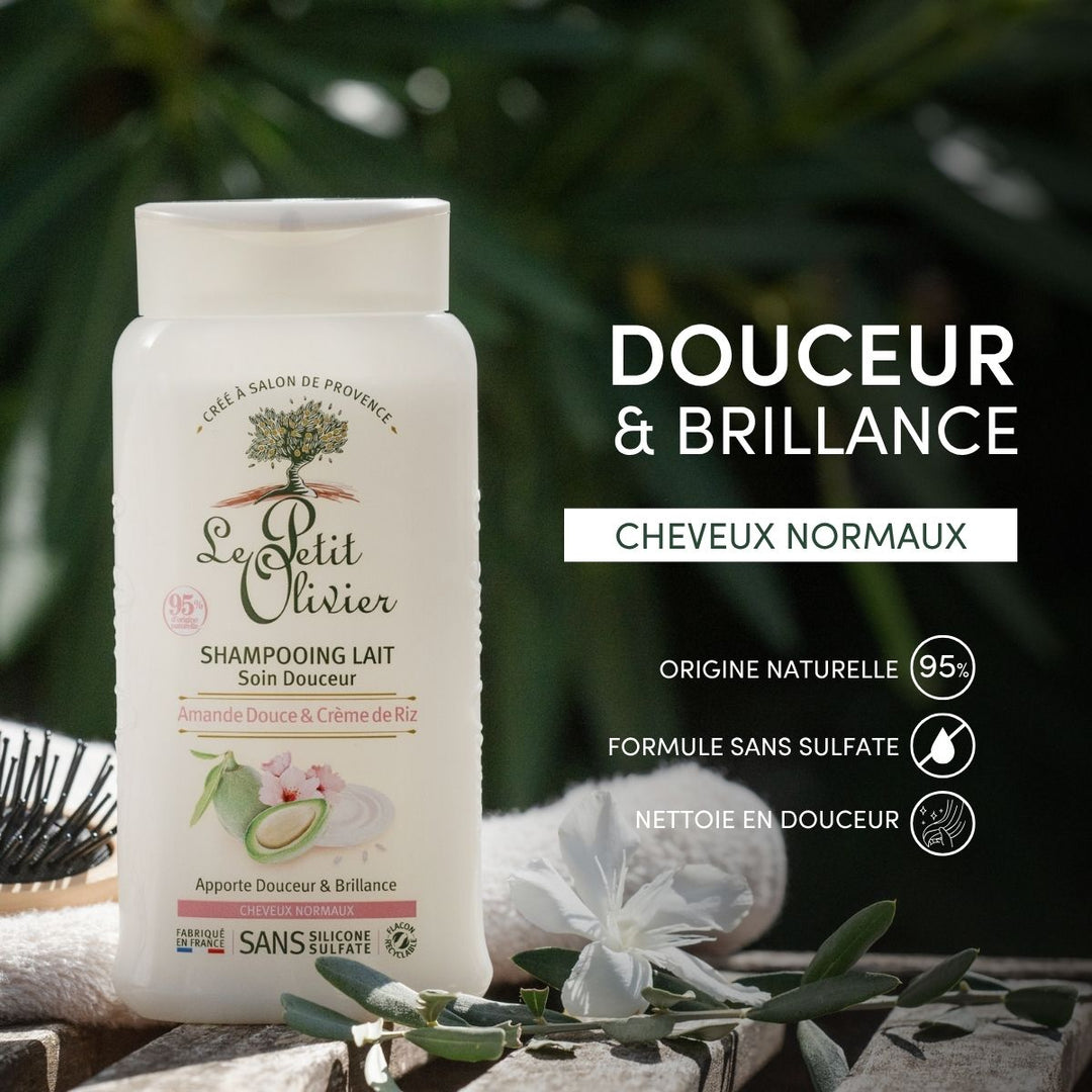 A bottle of Shampoing Cheveux Normaux sits outdoors among green leaves and white flowers, its label showcasing natural origins with amande douce, ideal for normal hair.
