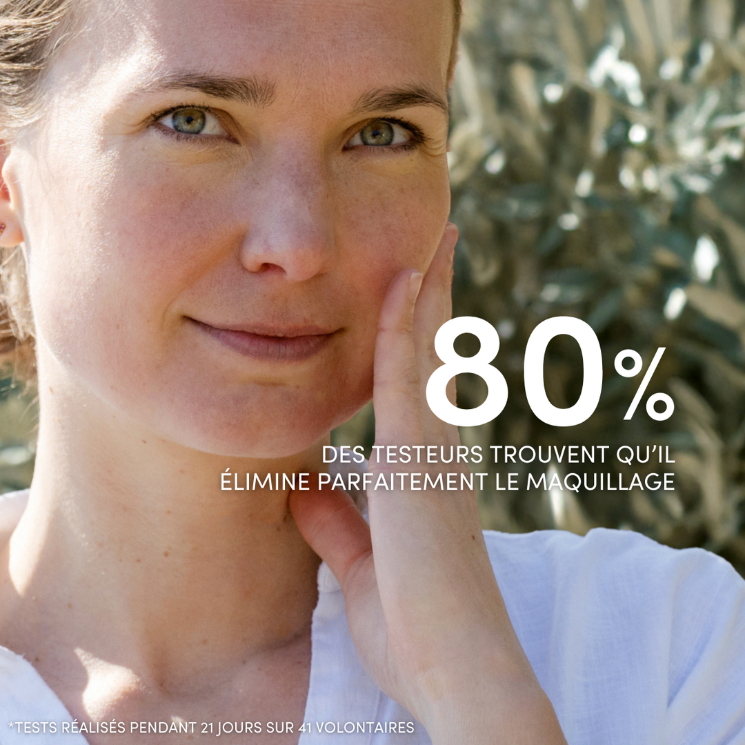 Une femme au teint clair se touche le visage en souriant. Légende en français : « 80 % des testeurs trouvent que le Démaquillant Yeux Sensibles Waterproof Le Petit Olivier élimine parfaitement le maquillage waterproof, même sur les yeux sensibles.* *Test de 21 jours, 41 volontaires. ».