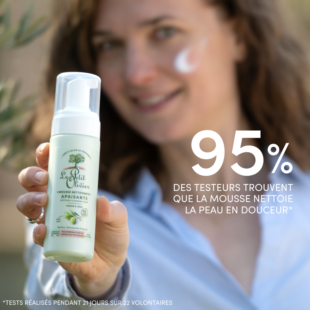 A smiling woman with foam on her cheek holds up a bottle of Mousse Nettoyante Visage Apaisante. Text reads: 95% des testeurs trouvent que la mousse nettoie la peau sèche en douceur.