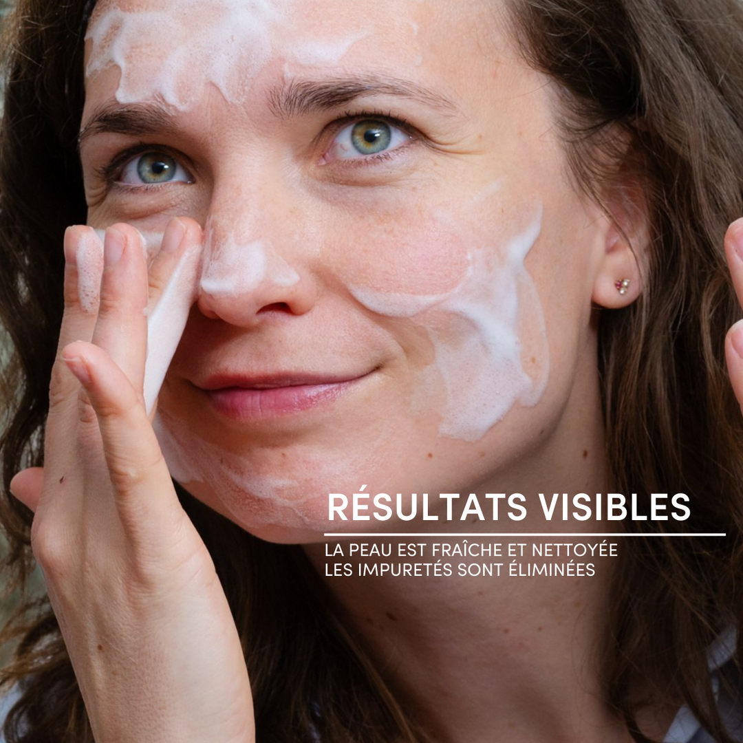 A woman uses Mousse Nettoyante Visage Apaisante on her face, softly massaging her cheek. French text reads: RÉSULTATS VISIBLES. La peau est fraîche et nettoyée. Les impuretés sont éliminées.