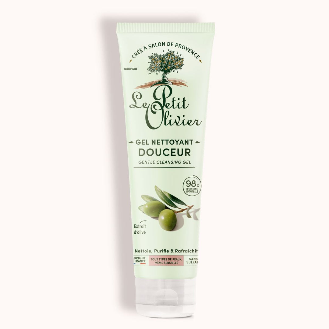 Le tube de gel nettoyant visage « Douceur » de Le Petit Olivier, destiné aux peaux sensibles, se présente dans un emballage vert clair orné d’olives et de feuilles, avec des mentions en français et en anglais soulignant que 98 % des ingrédients sont d’origine naturelle.