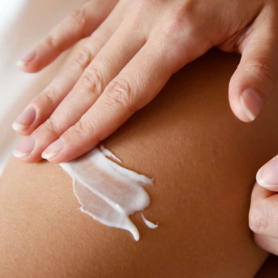 Gros plan sur une personne en train d'appliquer une lotion blanche sur sa peau, en l'étalant délicatement avec les doigts.