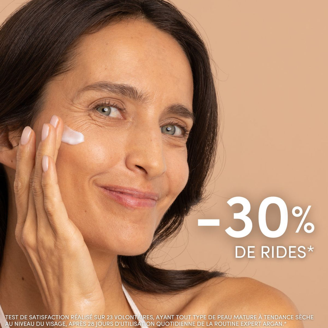 Une femme souriante aux longs cheveux châtains applique la Crème de Jour Anti-Âge Hydratante Le Petit Olivier sur sa joue. L'image porte la mention « -30 % de rides* ». Une petite mention relative au test de satisfaction français apparaît en bas de l'image.