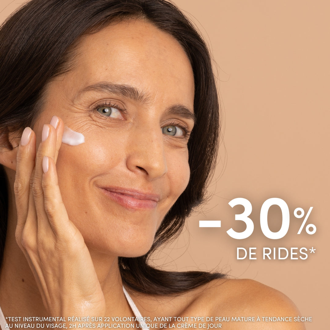 Une femme souriante aux longs cheveux châtains applique sur sa joue la « Duo Crème Jour et Baume Nuit Anti-âge » de Le Petit Olivier. Une grande inscription en français indique « -30 % de rides* », accompagnée d'une petite mention légale en bas de l'image.
