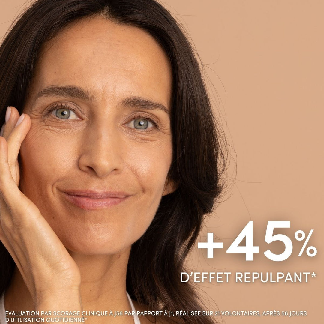 Une femme à la peau claire sourit doucement tout en se caressant le visage. Une inscription en blanc indique « +45 % d’effet repulpant* » au-dessus de « Baume de Nuit Anti-Âge Nourrissant, Le Petit Olivier », suggérant une peau plus rebondie et des bienfaits anti-âge visibles.