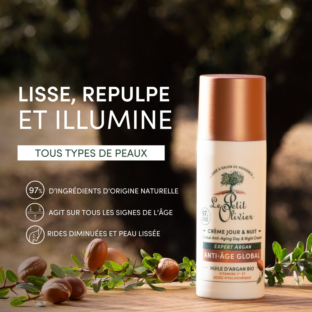 Un flacon de « Le Petit Olivier Crème Hydratante Jour & Nuit Anti-Âge » repose sur un socle en bois orné de noix et de feuilles d'argan, au milieu d'une végétation luxuriante. Le texte en français met en avant l'acide hyaluronique, l'huile d'argan et les propriétés anti-âge naturelles adaptées à tous les types de peau.