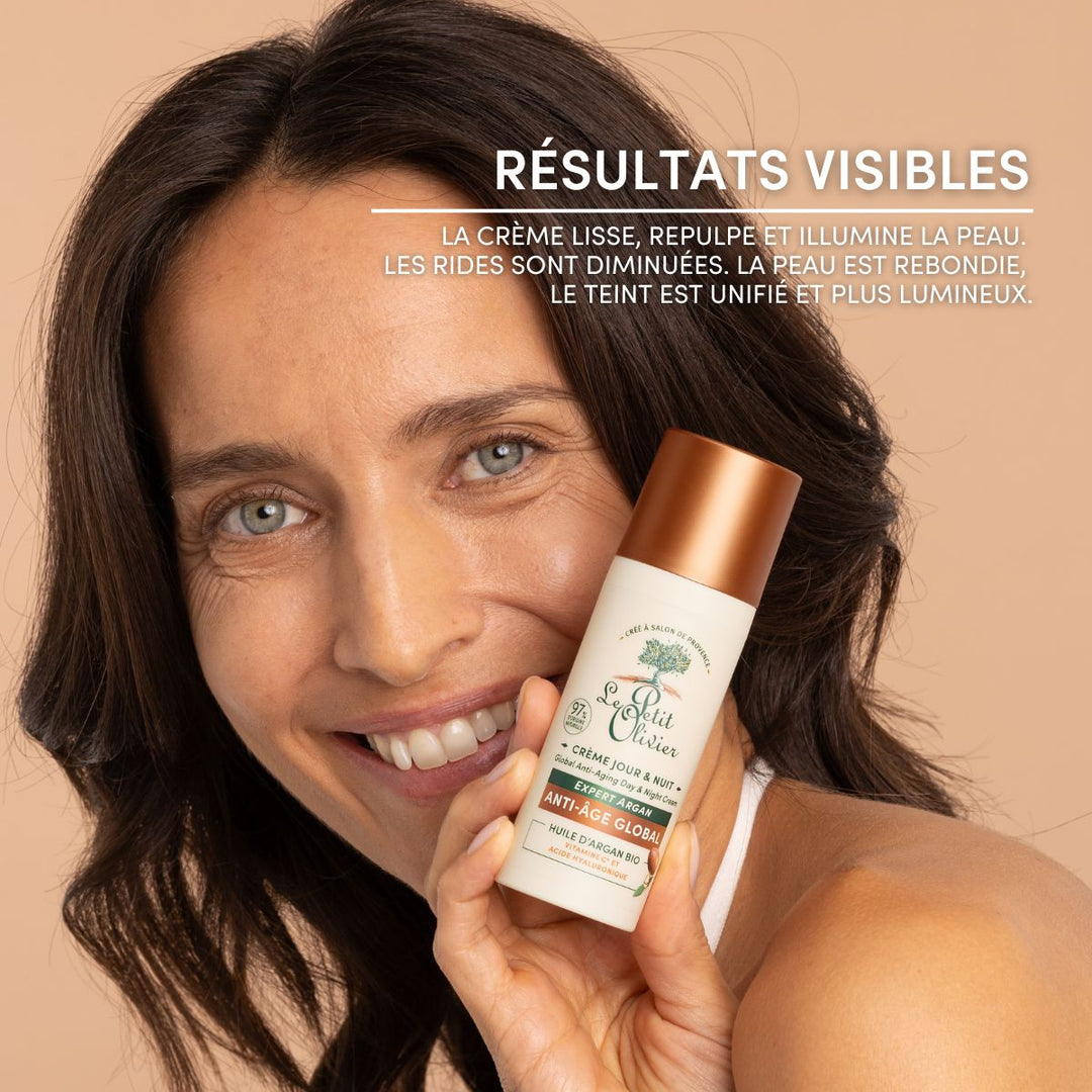 Une femme souriante, aux yeux clairs et aux cheveux bruns ondulés, tient en main la crème « Le Petit Olivier Crème Hydratante Jour & Nuit Anti-Âge ». Le texte en français met en avant des résultats visibles : une peau plus lisse, plus rebondie et plus éclatante, avec moins de rides et un teint plus uniforme.