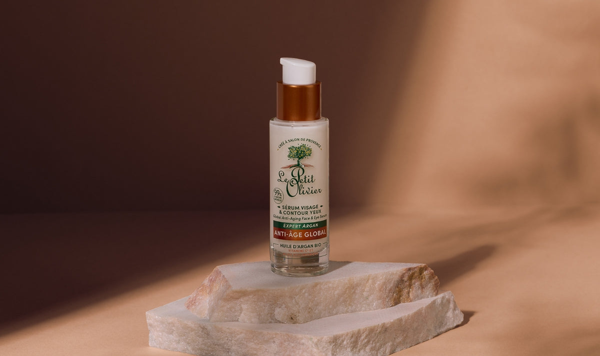 Un flacon de sérum anti-âge « Le Petit Olivier », muni d'un doseur à pompe, est posé sur une pierre blanche devant un fond beige.