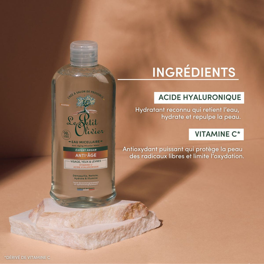 Un flacon d'Eau Micellaire Anti-Âge de Le Petit Olivier est posé sur une pierre, devant un fond beige. Le texte met en avant l'acide hyaluronique pour l'hydratation et la vitamine C* pour la protection antioxydante.