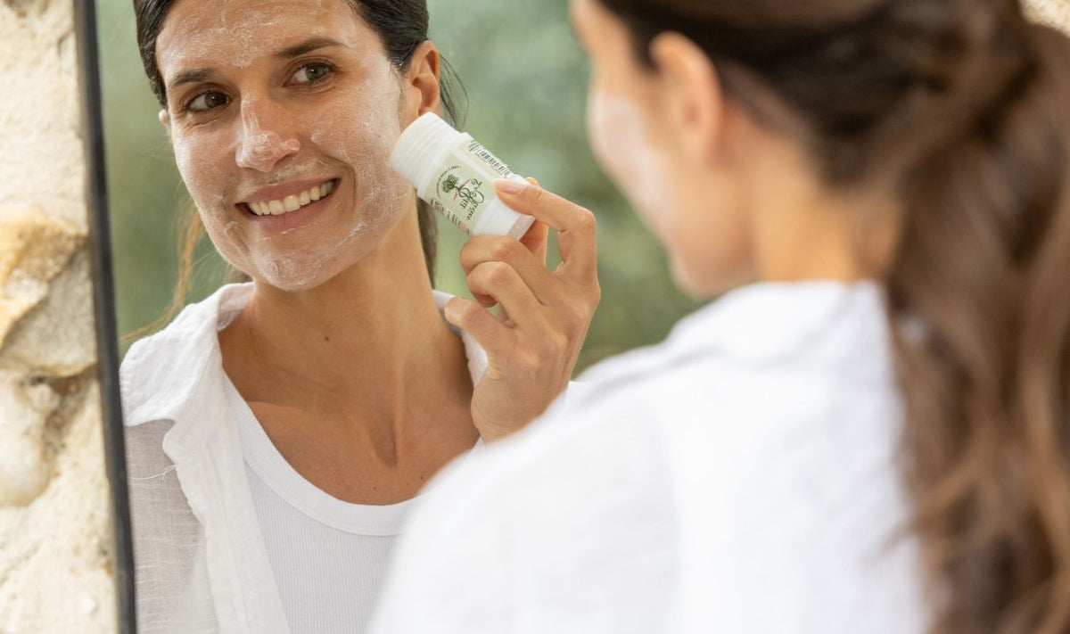 femme souriante appliquant un masque stick à l'argile blanche sur son visage