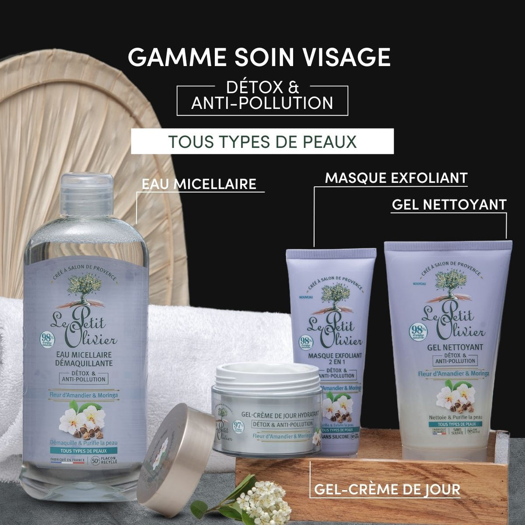 A set of Le Petit Olivier skincare for all skin types is showcased on a black surface, featuring Eau Micellaire Démaquillante Detox & Anti-Pollution, exfoliating mask, cleansing gel, and day gel-cream with wood and green leaves in the background.