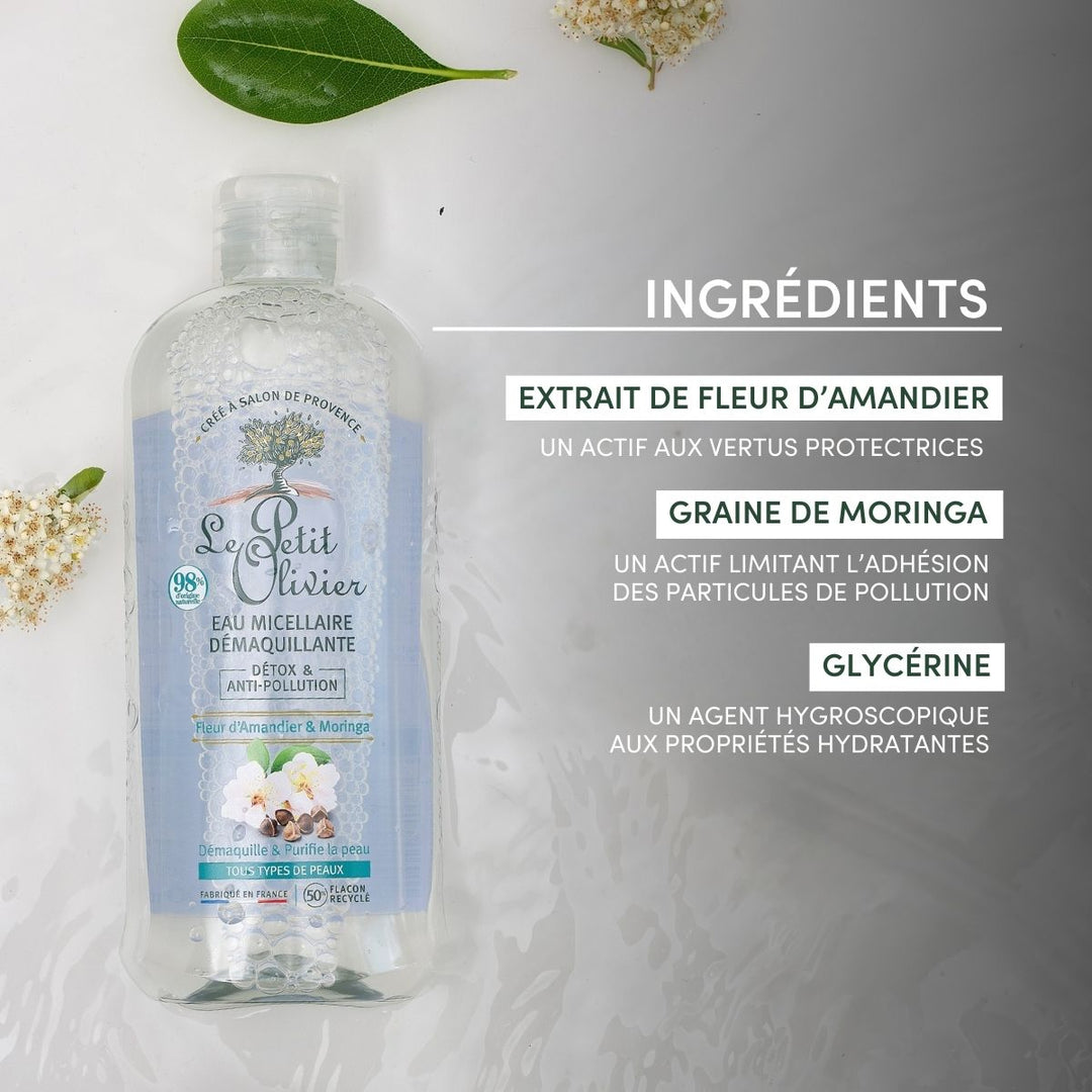 A bottle of Eau Micellaire Démaquillante Detox & Anti-Pollution sits on a light surface with white flowers and green leaves. Its anti-pollution benefits are listed in French on a soft gray background.
