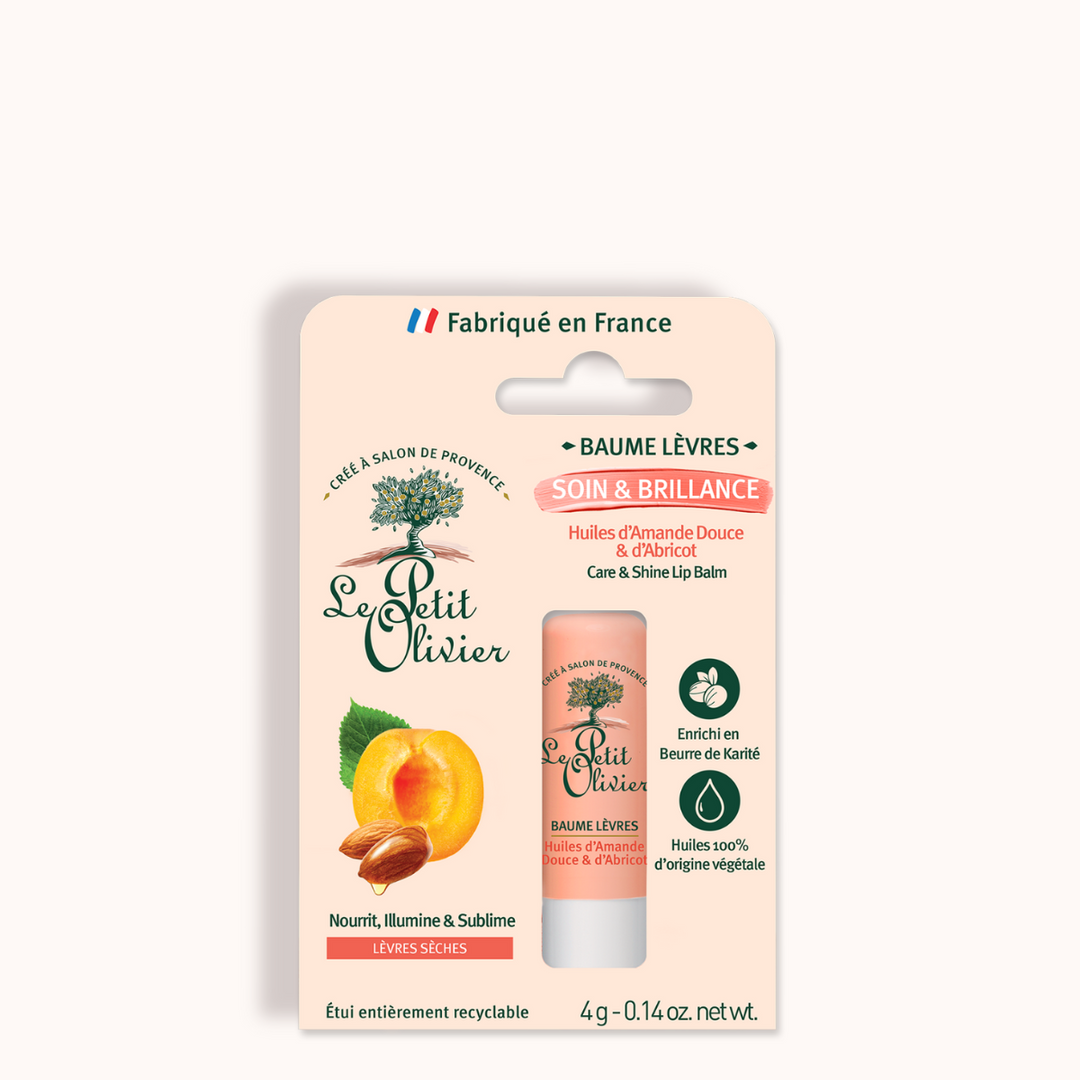 A packaged Baume Lèvres Soin & Brillance for dry lips with almond, apricot oils, and shea butter. The mostly white pack displays an apricot, product tube, green olive tree logo, and French text.
