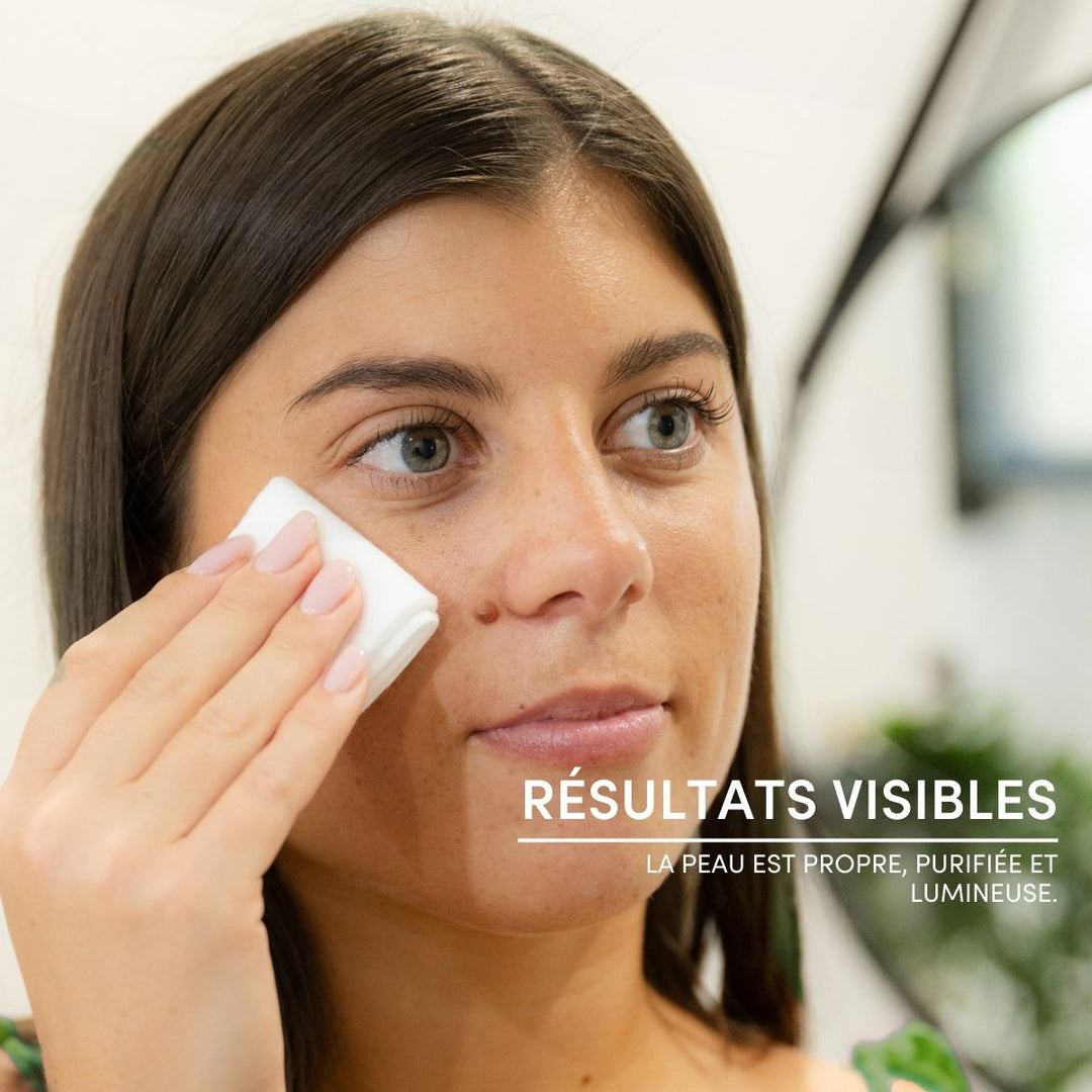 A woman applies Gelée Micellaire Démaquillante Visage & Yeux to her cheek with a cotton pad while looking in the mirror. French text reads, RÉSULTATS VISIBLES. La peau est propre, purifiée et lumineuse.