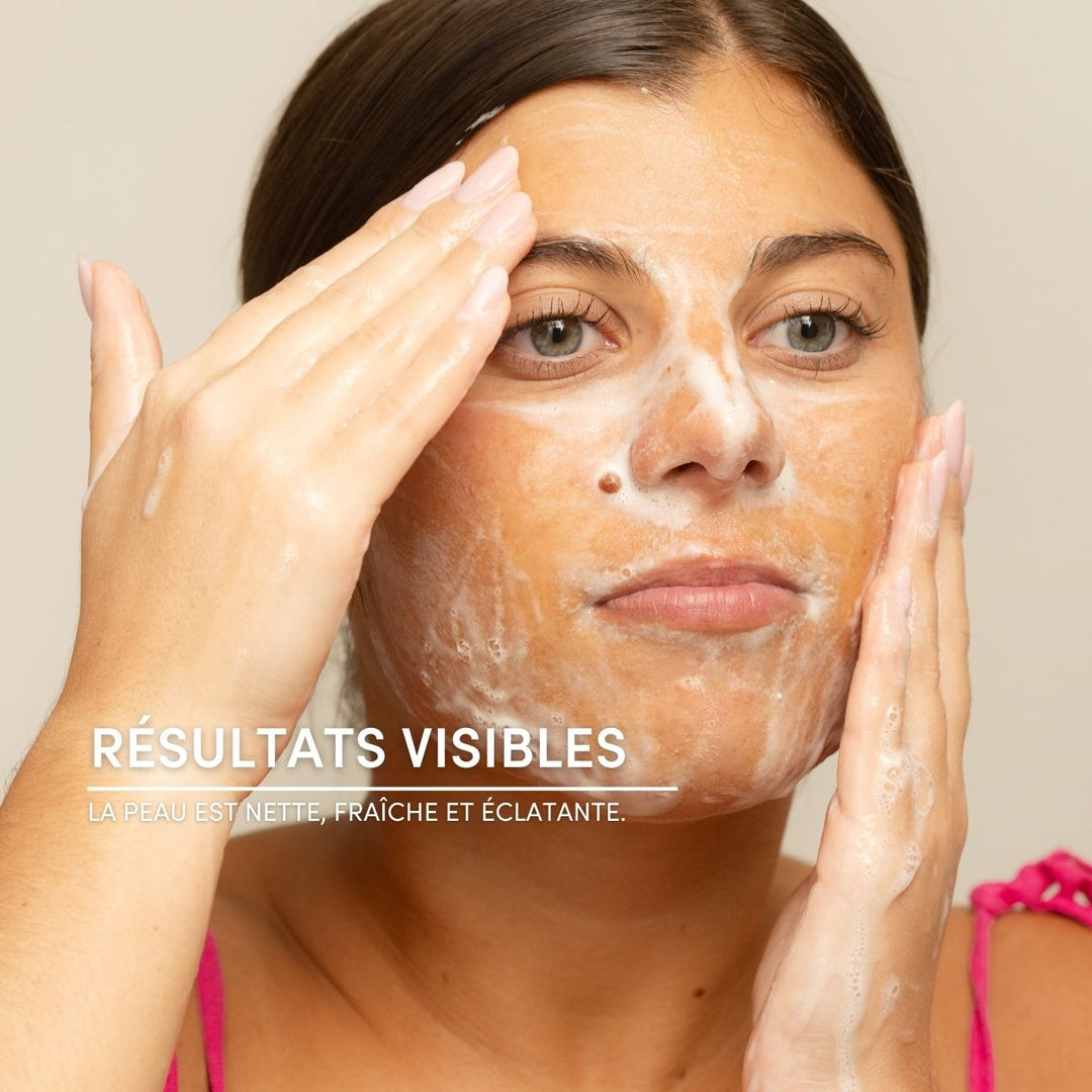 Une femme applique le gel nettoyant exfoliant Le Petit Olivier sur son visage, formant ainsi une mousse onctueuse. Le texte en français indique : « RÉSULTATS VISIBLES : La peau est nette, fraîche et éclatante. » Elle montre comment utiliser ce produit de soin.