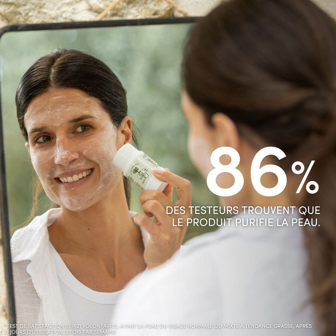 Une femme sourit en appliquant le « Masque Visage Stick Pureté » de Le Petit Olivier sur sa joue devant un miroir. Une légende indique : « 86 % des testeurs trouvent que le produit purifie la peau. » Un paysage naturel est visible en arrière-plan.