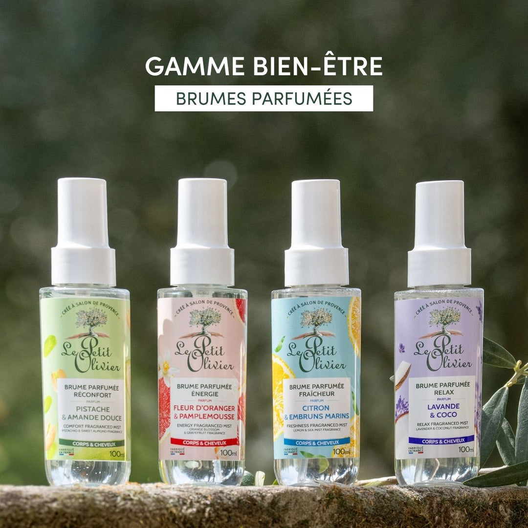 Quatre flacons de « Le Petit Olivier Brume Parfumée Énergie » sont présentés en extérieur sur une surface en pierre ; ils déclinent des parfums tels que pistache, fleur d’oranger et pamplemousse, citron et minéraux marins, ainsi que lavande et noix de coco.