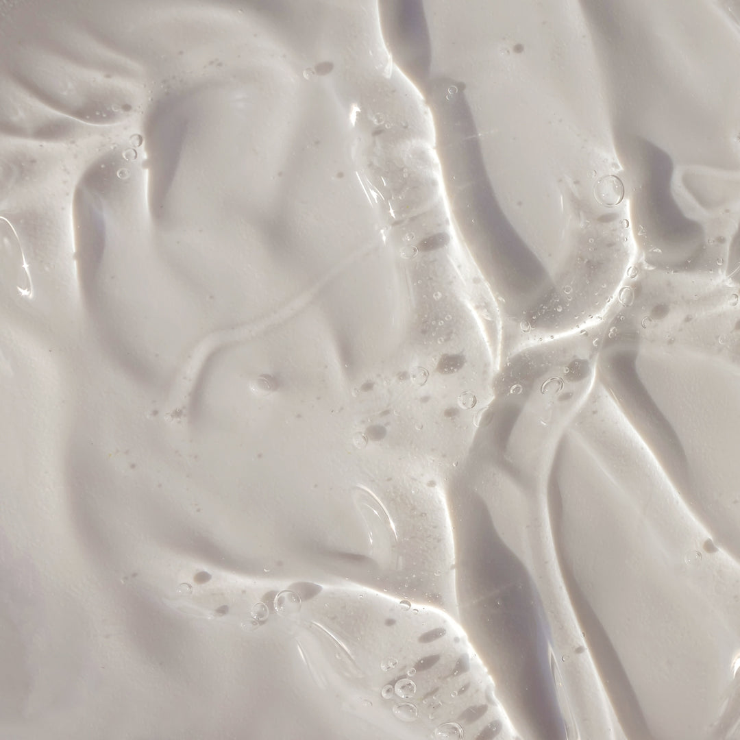 Gros plan sur un liquide blanc et onctueux, parsemé de bulles et à la texture veloutée, qui évoque le « Duo Savon Liquide & Recharge - Sans Parfum » de Le Petit Olivier — idéal pour les peaux sensibles et qui rappelle les soins doux pour la peau.