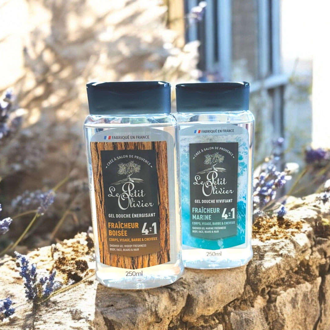 Deux flacons de « Le Petit Olivier Duo Gel Douche Homme 4 en 1 » sont posés sur un rebord en pierre à l'extérieur, entourés de fleurs de lavande.