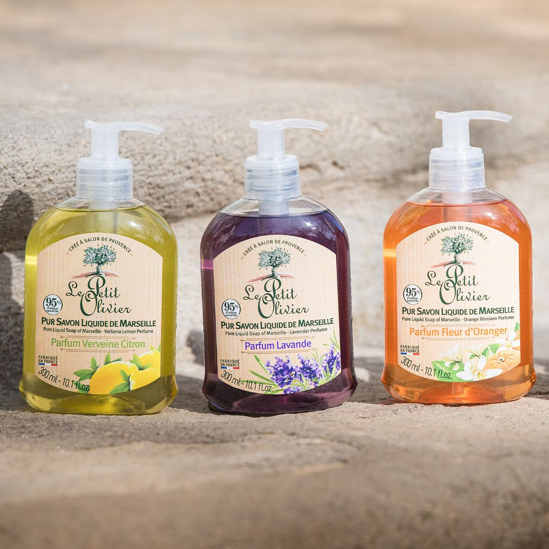 Trois flacons issus du coffret « Découverte » de Le Petit Olivier – « Purs Savons Liquides de Marseille » – sont exposés à l'extérieur ; chacun d'entre eux est fabriqué selon des méthodes traditionnelles et se décline dans les parfums Verveine Citron (jaune), Lavande (violet) et Fleur d’Oranger (orange).