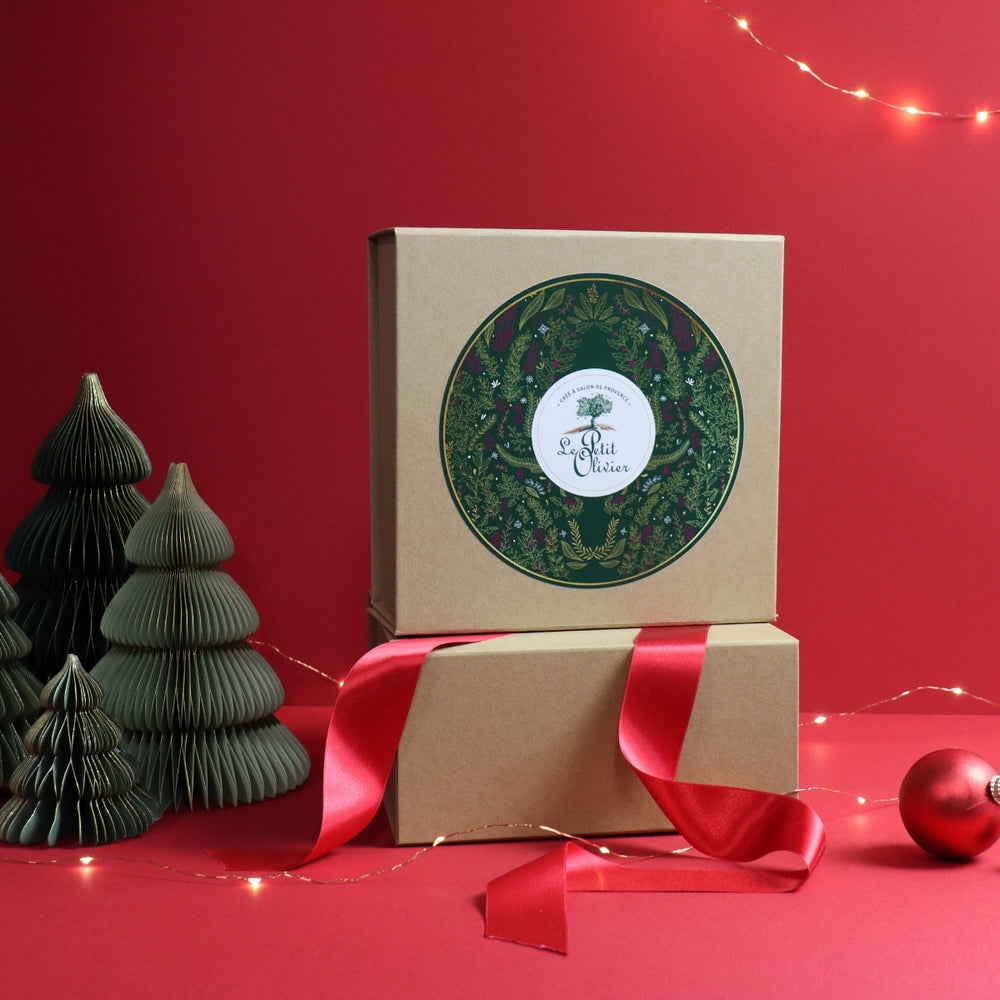 Deux coffrets cadeaux de Noël marron de la marque Le Petit Olivier sont empilés sur un fond rouge ; chacun est orné d'une étiquette en forme de couronne verte, d'un ruban rouge festif, de sapins de Noël en papier, d'une décoration rouge et d'une guirlande lumineuse. Fabriqué en France.