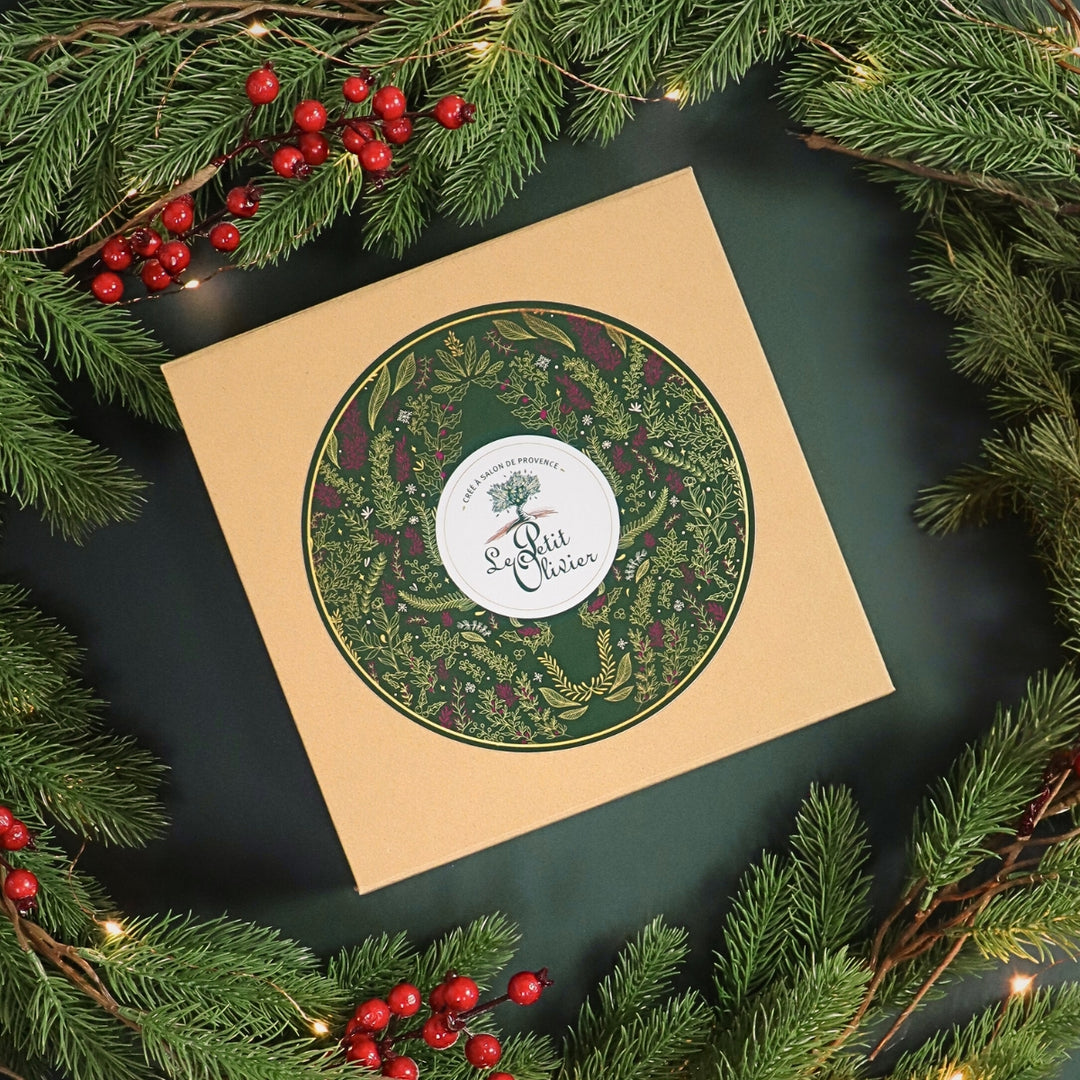 Le coffret cadeau de Noël de Le Petit Olivier, avec son motif botanique vert et or, est agrémenté de branches de sapin, de baies rouges et de guirlandes lumineuses pour créer une ambiance festive.