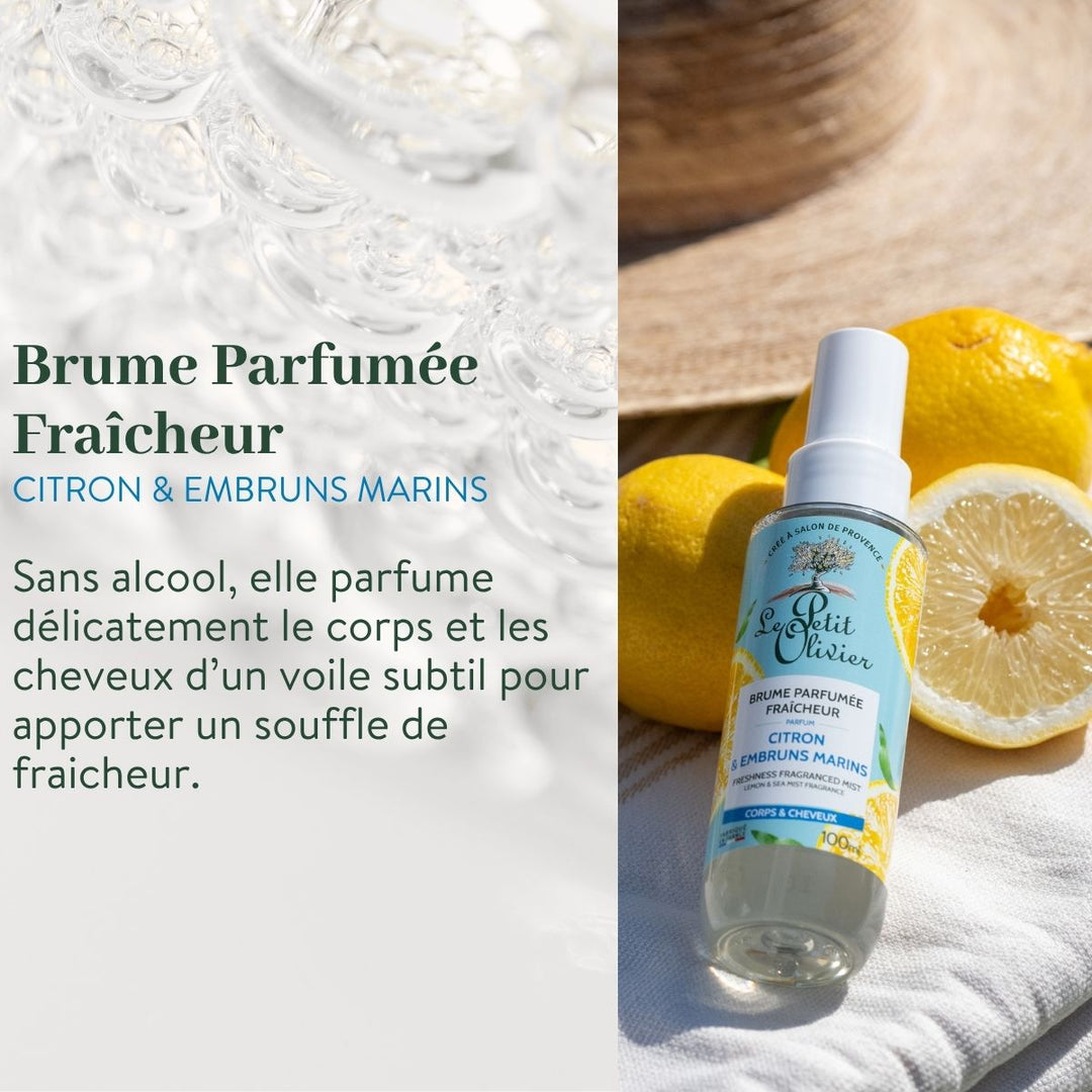 Un flacon de « Le Petit Olivier Duo Fraîcheur - Gel Douche et Brume Parfumée » repose sur un tissu blanc, accompagné de citrons et d'un chapeau de paille ; la lumière du soleil met en valeur la fraîcheur éclatante et les notes de citron et de mer de cet ensemble rafraîchissant de brume pour le corps.