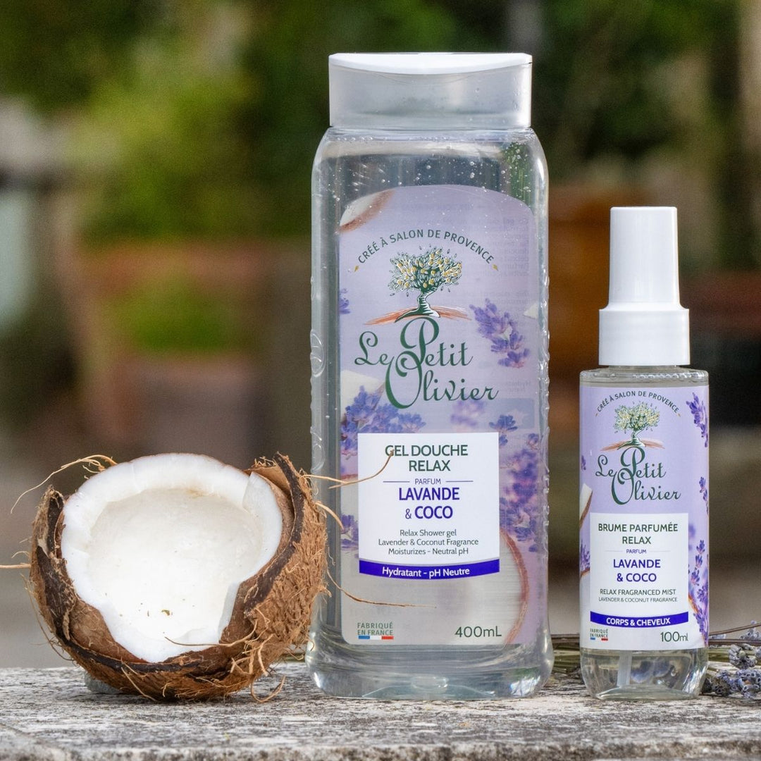 Le « Duo Relax » de Le Petit Olivier – gel douche et brume parfumée – est présenté en extérieur sur une surface rustique, à côté d'une noix de coco coupée en deux, sur un fond vert légèrement flou.
