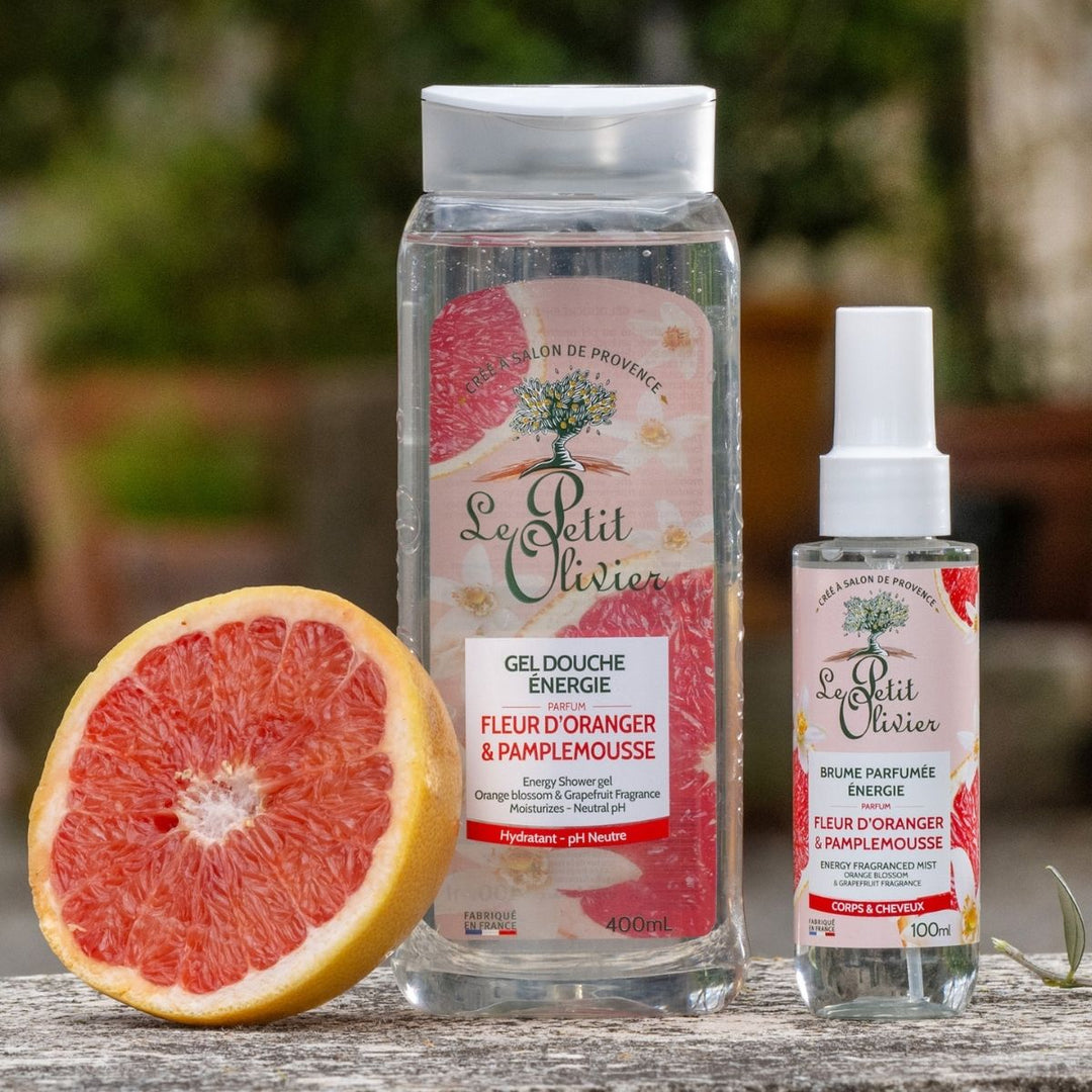 Le duo « Énergie » de Le Petit Olivier – gel douche et brume parfumée à la fleur d'oranger et au pamplemousse – est présenté en extérieur, à côté d'un demi-pamplemousse.