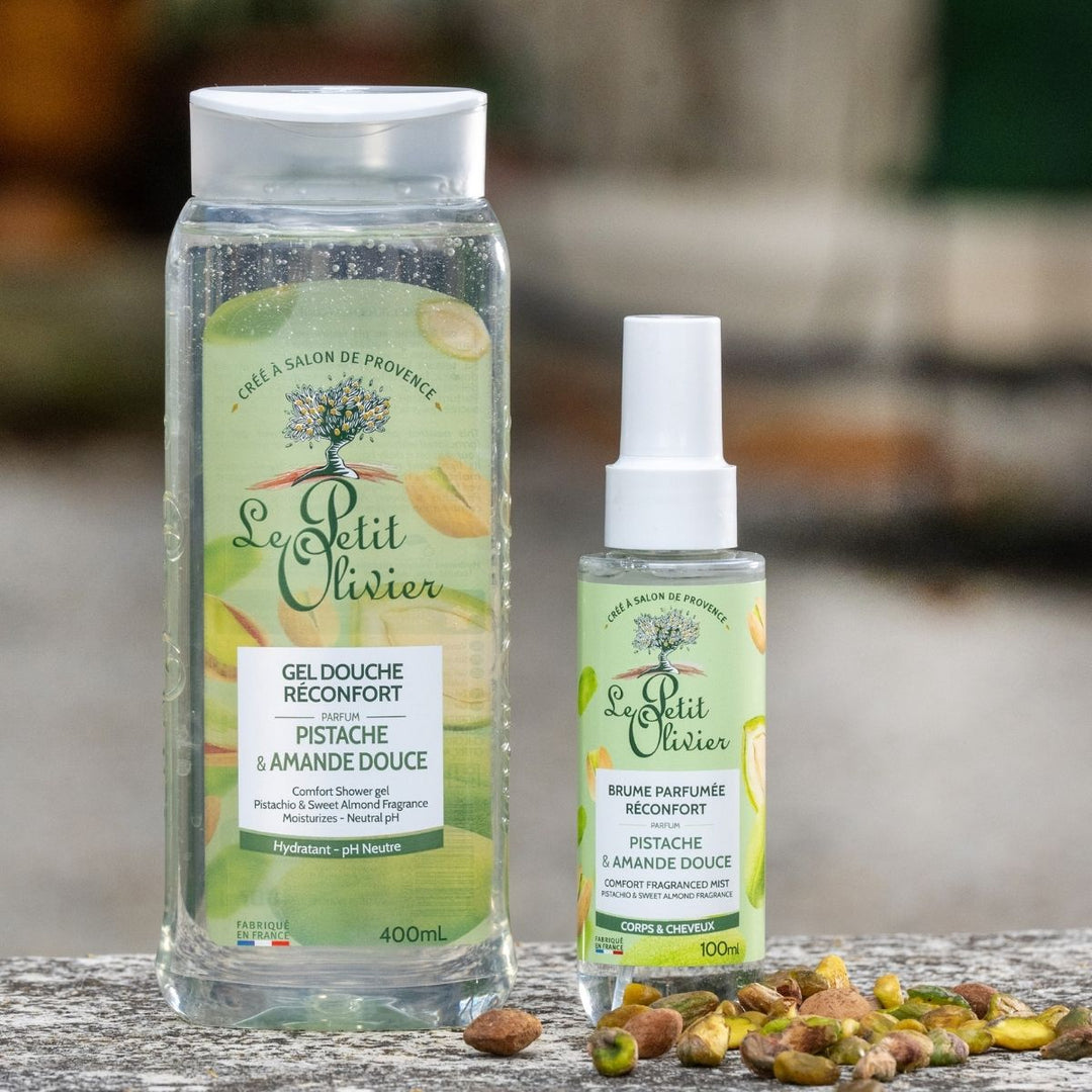 Le « Duo Réconfort » de Le Petit Olivier — gel douche et brume parfumée — est présenté sur une surface en pierre, avec des pistaches au premier plan et un arrière-plan flou.