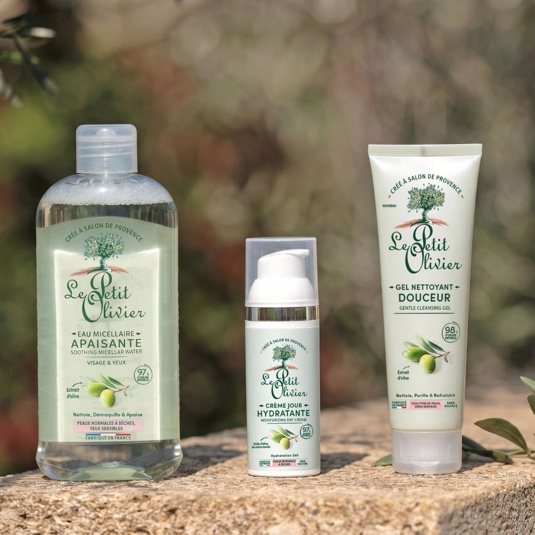 Le coffret de soins « Rituel Soin Visage Express Douceur » de Le Petit Olivier, enrichi en extraits d'olive et destiné aux peaux normales à sèches, est présenté en extérieur sur un rebord en pierre, avec un fond vert flou en arrière-plan.