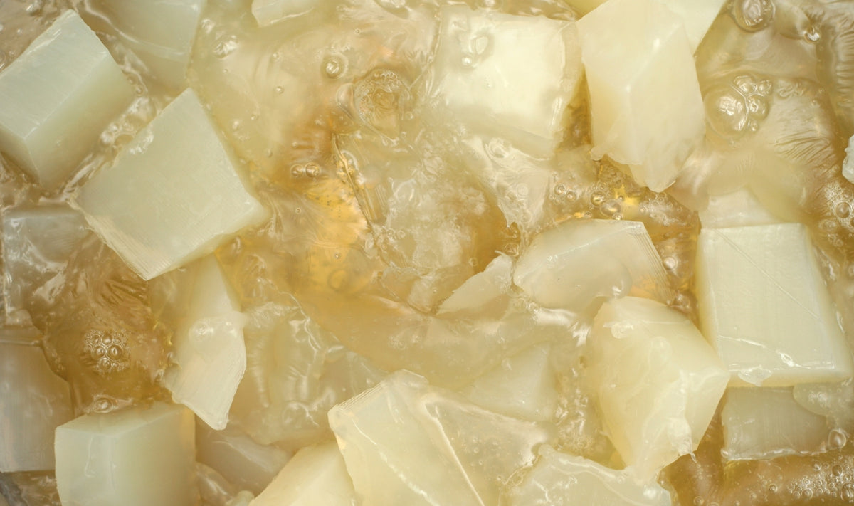 Gros plan sur des cubes blancs translucides de nata de coco en suspension dans un sirop clair, légèrement jaunâtre, parsemé de bulles. L'image met en valeur la texture et la surface brillante de ce dessert sucré à base de gel de noix de coco.