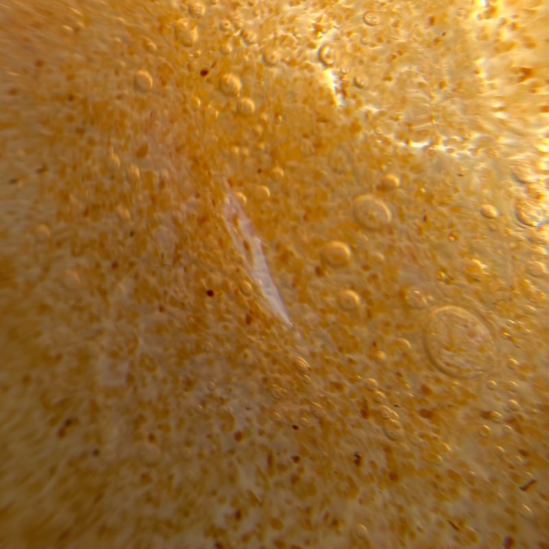 Gros plan sur une surface texturée, de couleur jaune-orange, présentant de petites protubérances circulaires et des taches éparses, qui rappelle un matériau cratérisé ou alvéolé.
